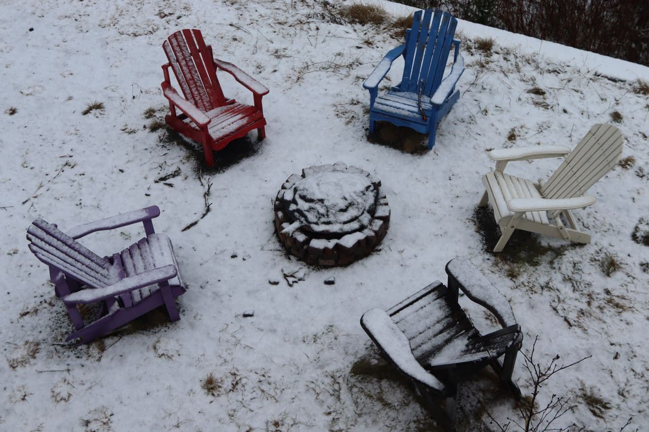 Snow-covered outdoor chairs around a fire pit on a winter day
