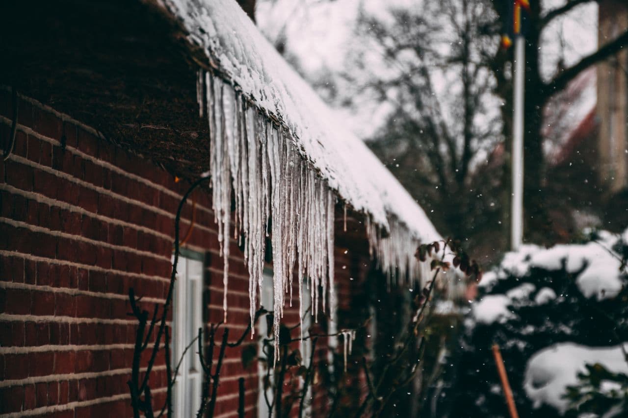 Icicles hanging from the snowy roof edge of a brick house in winter