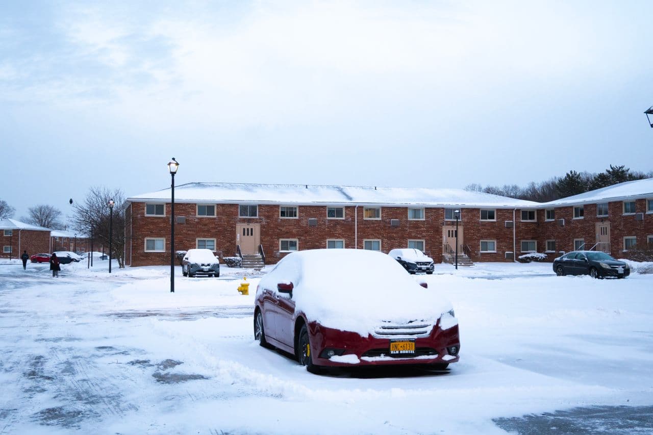 A snowy residential street with parked cars on a winter morning