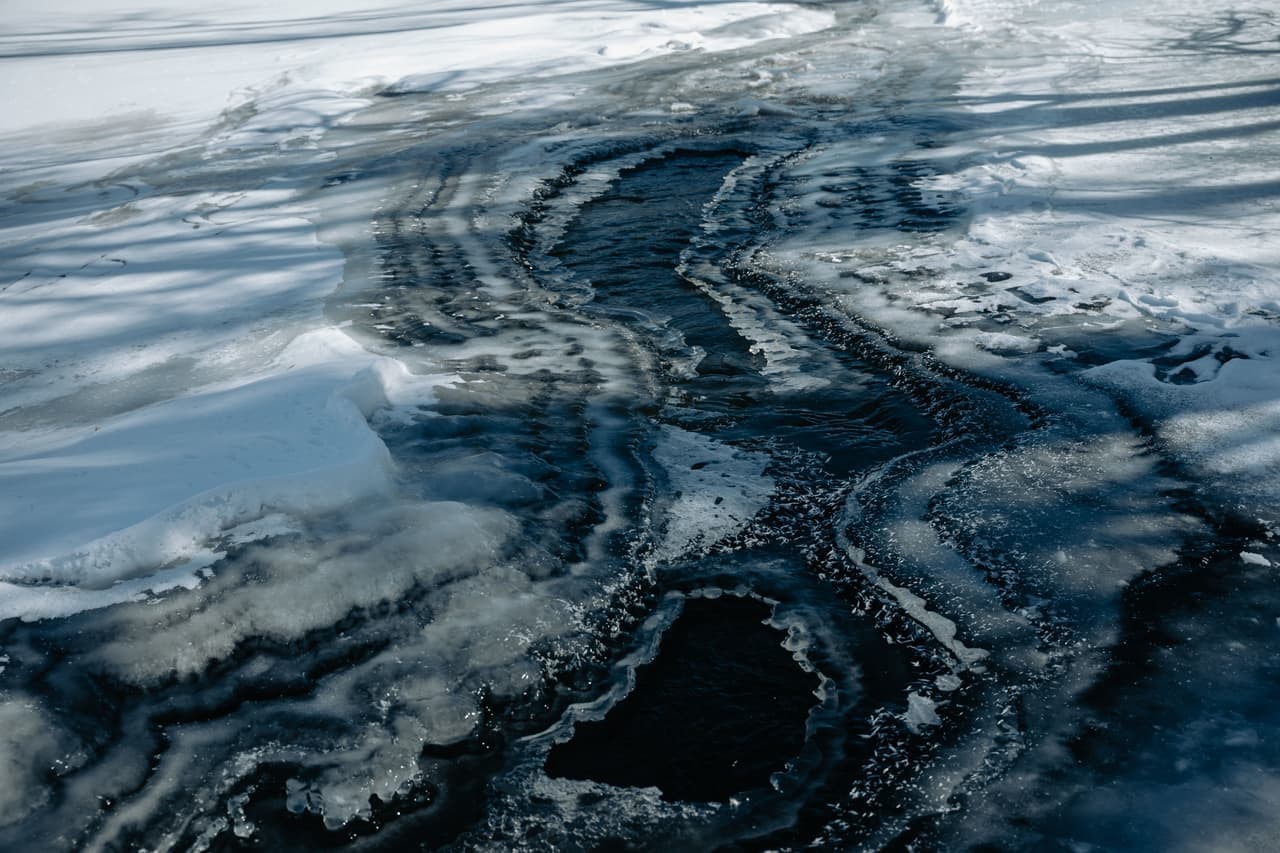 A cleared driveway with meltwater running toward a drain at the low edge