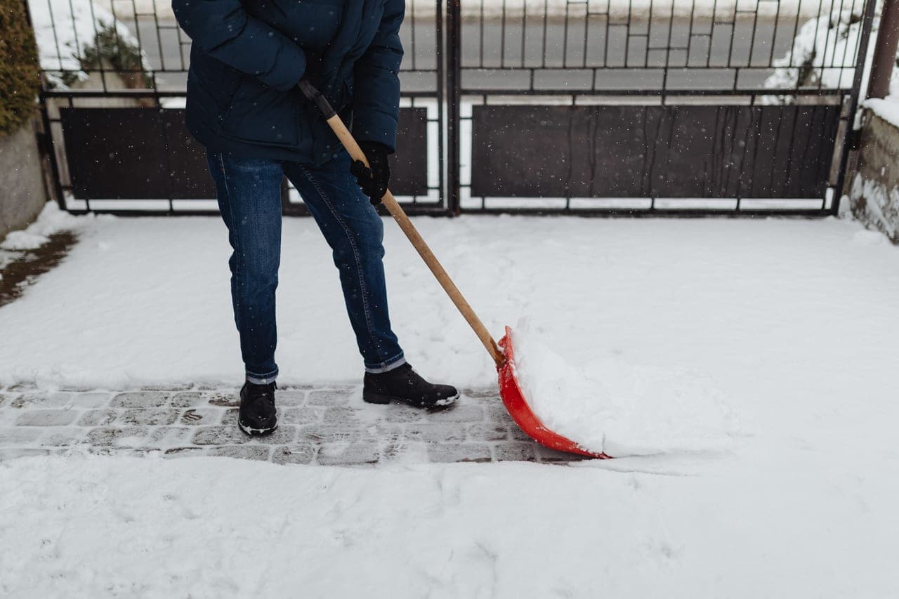 A snow shovel and a snow blower side by side on a partly cleared driveway