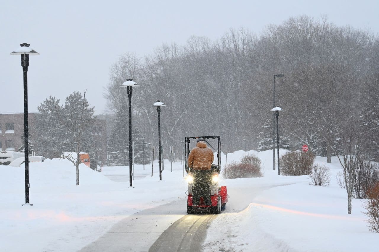 An operator on a compact ride-on machine clearing a path through heavy snowfall