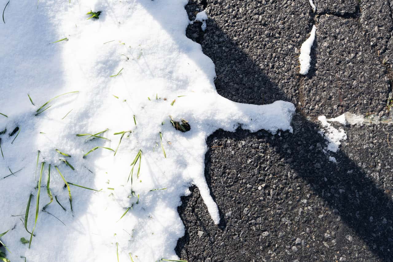 A dark asphalt driveway partially cleared of snow with treated patches