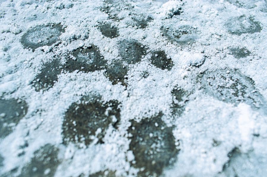 Close-up of white salt crystals scattered across a dark paved surface
