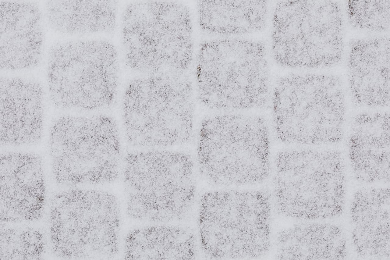 Snow partially cleared from an interlocking paver driveway showing the joint pattern
