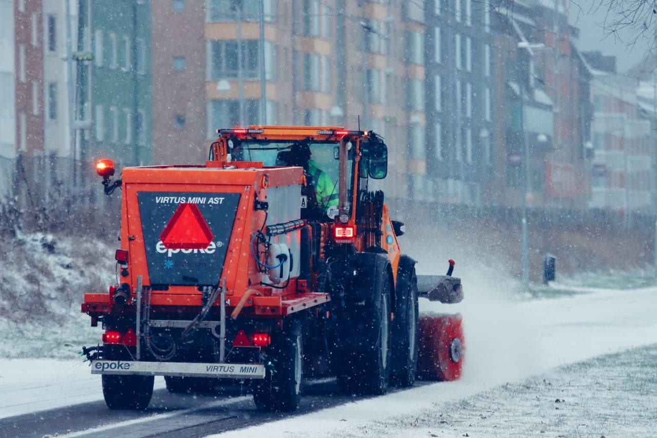 A cordless snow blower with battery packs fitted, standing on cleared pavement