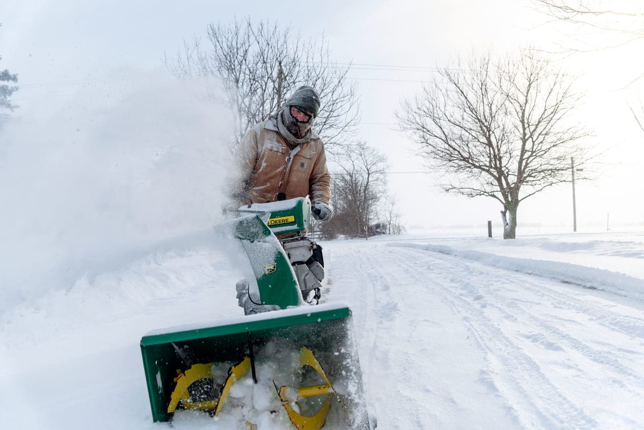 A snow blower parked at the end of a freshly cleared driveway in winter