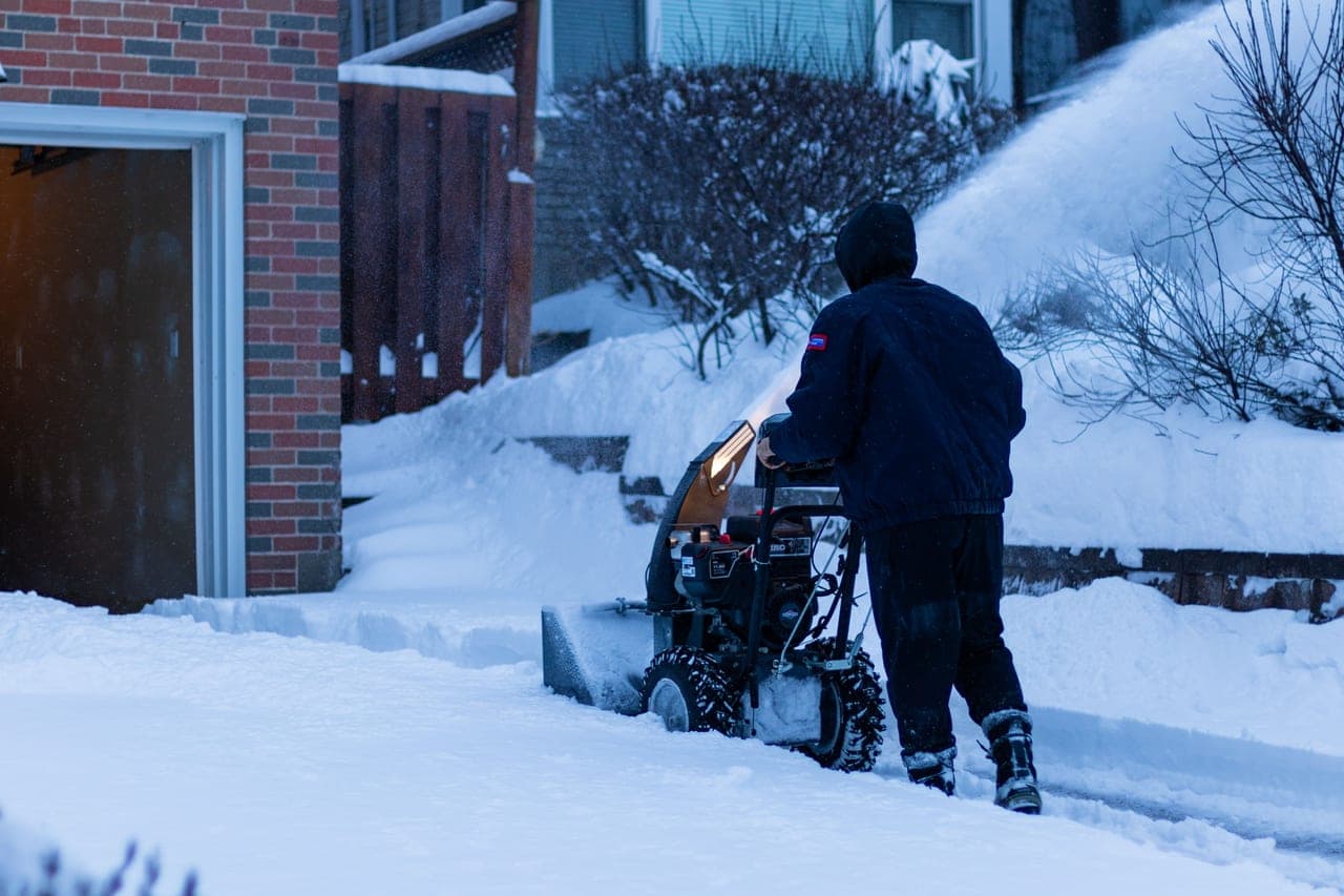An electric snow blower clearing a wide path across a snow-covered driveway