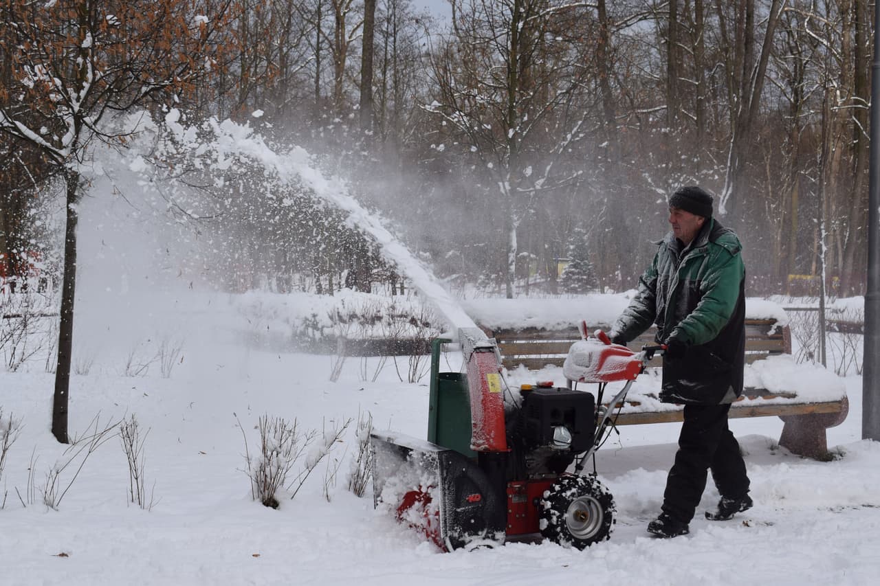 A snow blower parked beside a partly cleared driveway in winter