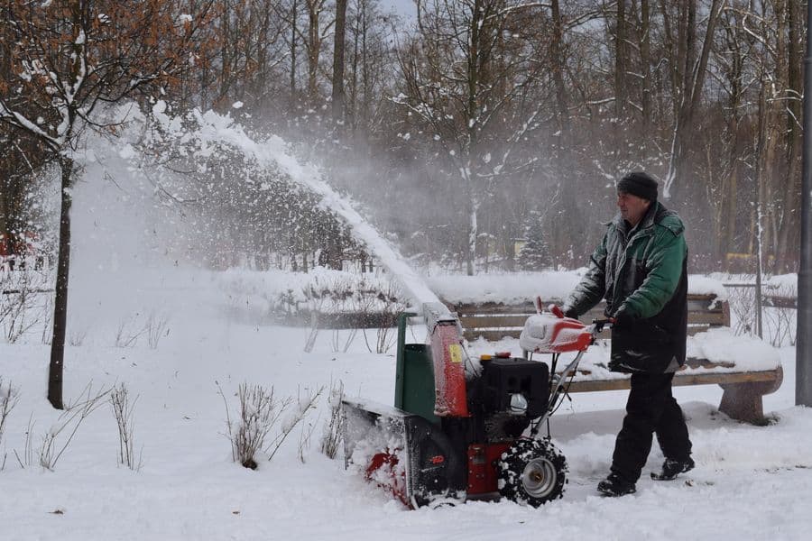 A person in a green jacket clearing snow with a snow blower