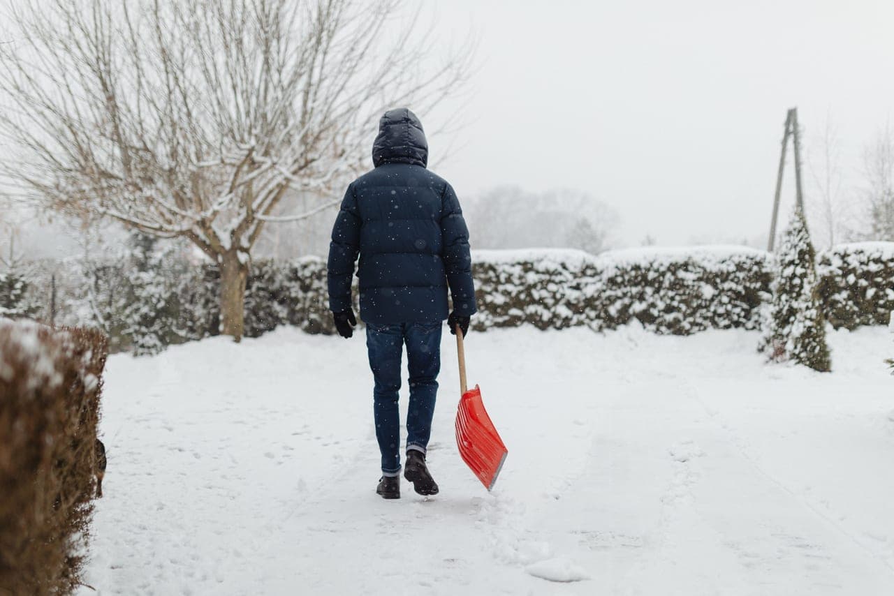 A person clearing fresh snow from a driveway with a long-handled snow shovel