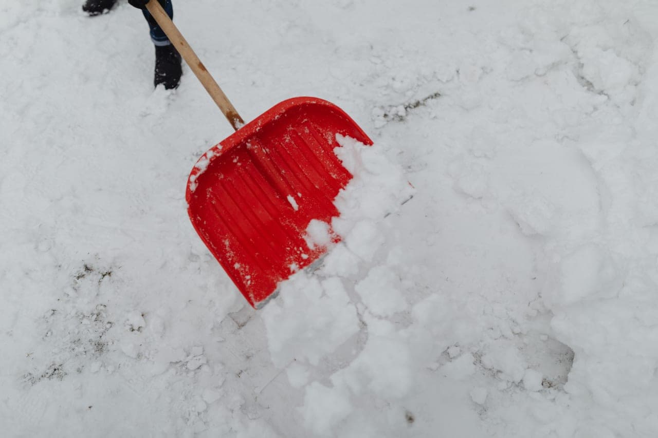 A bent-shaft snow shovel resting against a snowbank beside a cleared path