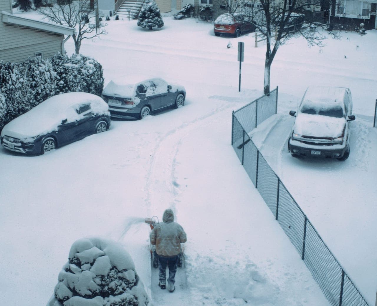 A wide snow pusher clearing a straight strip across a snow-covered driveway