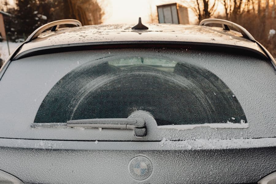 Close-up of a frosted car window covered with snow, with the wiper visible
