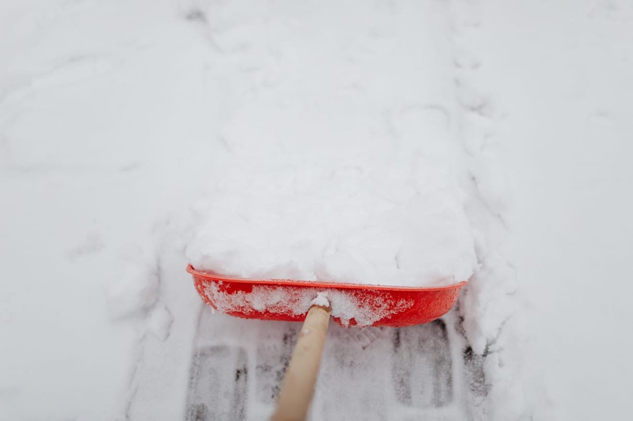 A snow shovel standing upright in deep fresh snow beside a cleared driveway path